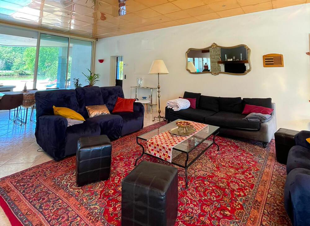 Salle à manger et salon de détente avec canapés, grande table pour manger en famille ou entre amis, piscine et jardin en fond