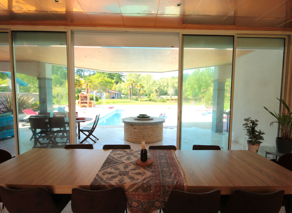 Salon avec grande table pour manger en famille ou entre amis, jardin et parc et piscine en fond